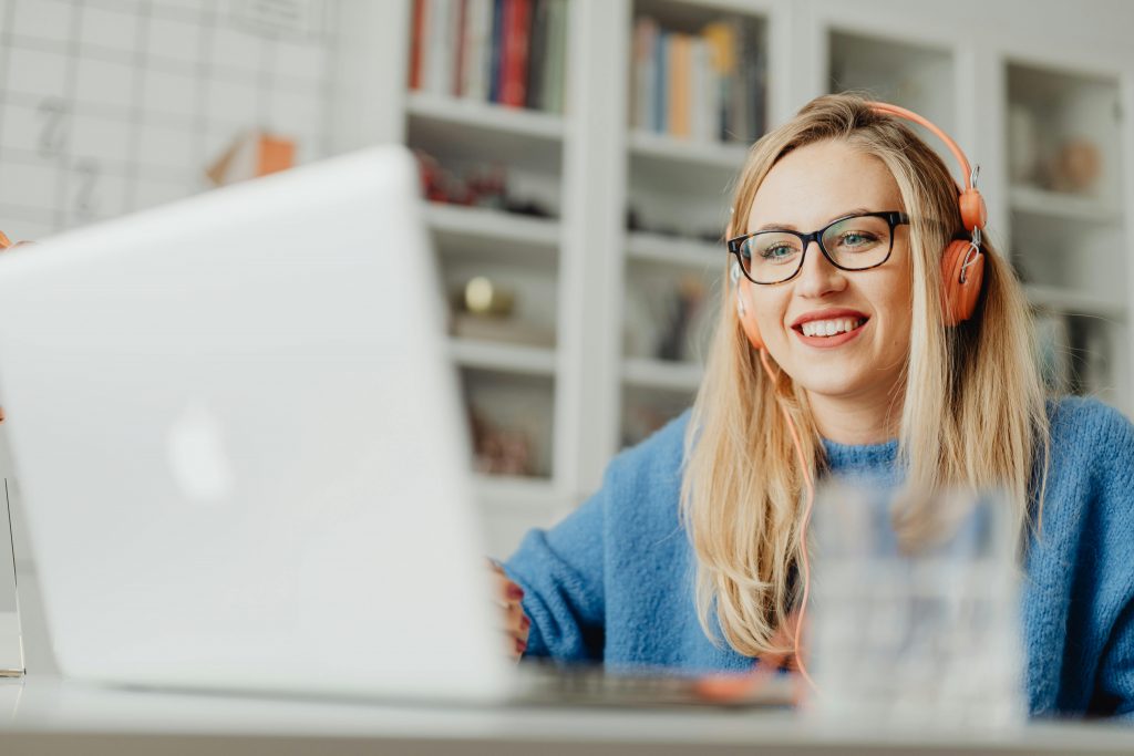 woman wearing a blue sweater, eyeglasses, and peach headphones smiling while in a virtual meeting